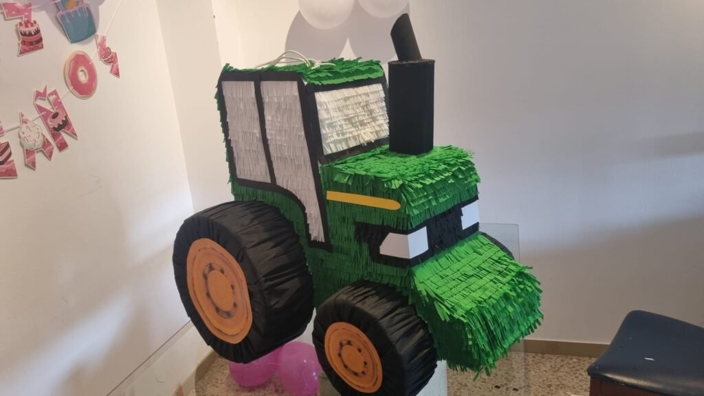 Piñata en forma de tractor verde con detalles en negro y amarillo, decorando un espacio festivo.